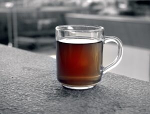 Tazza di tè rooibos rosso con foglie secche e un cucchiaino, evidenziando i suoi benefici antiossidanti.